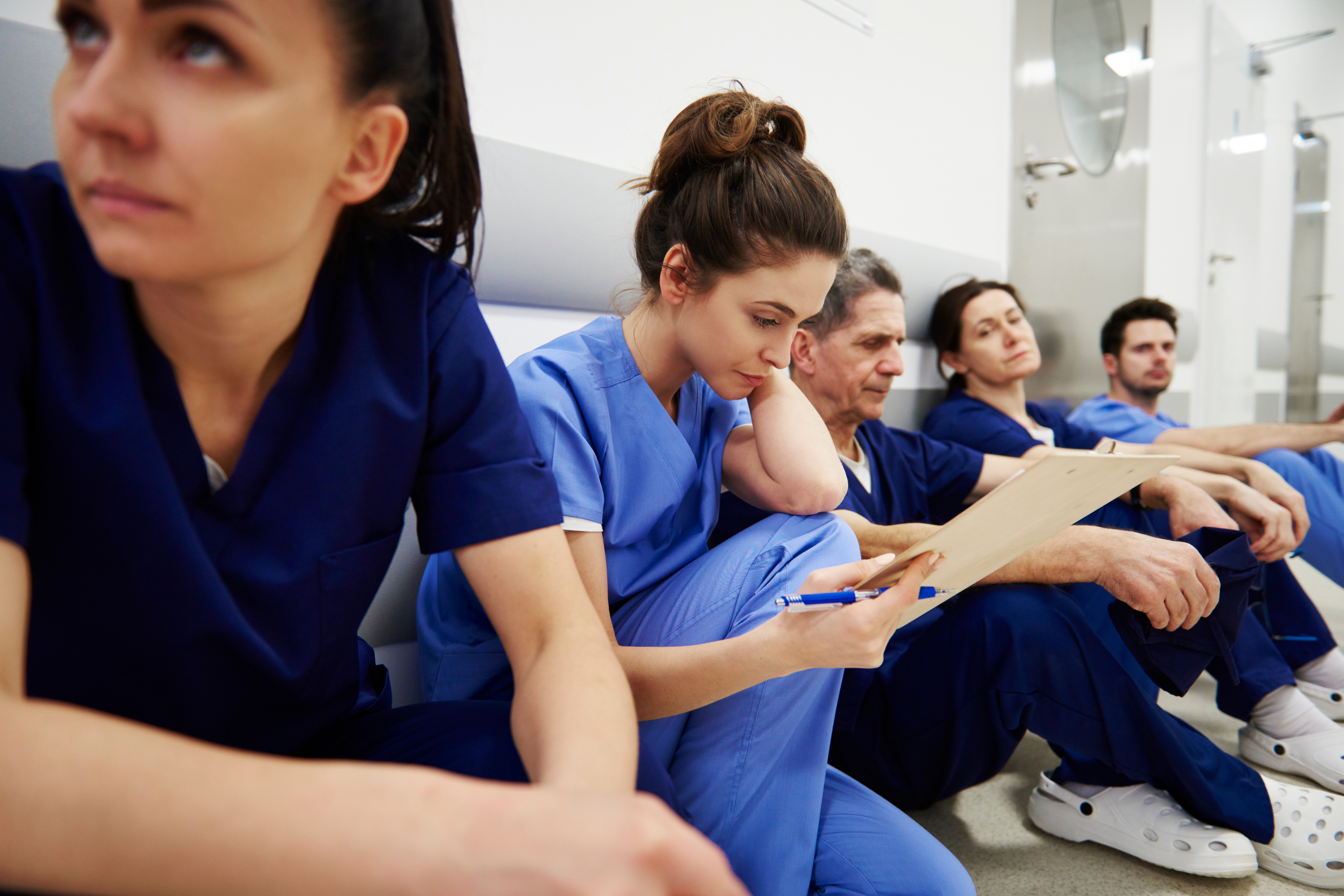 Nurses seated in a corridor taking a break from a busy day. One nurse examines medical records in the corridor.